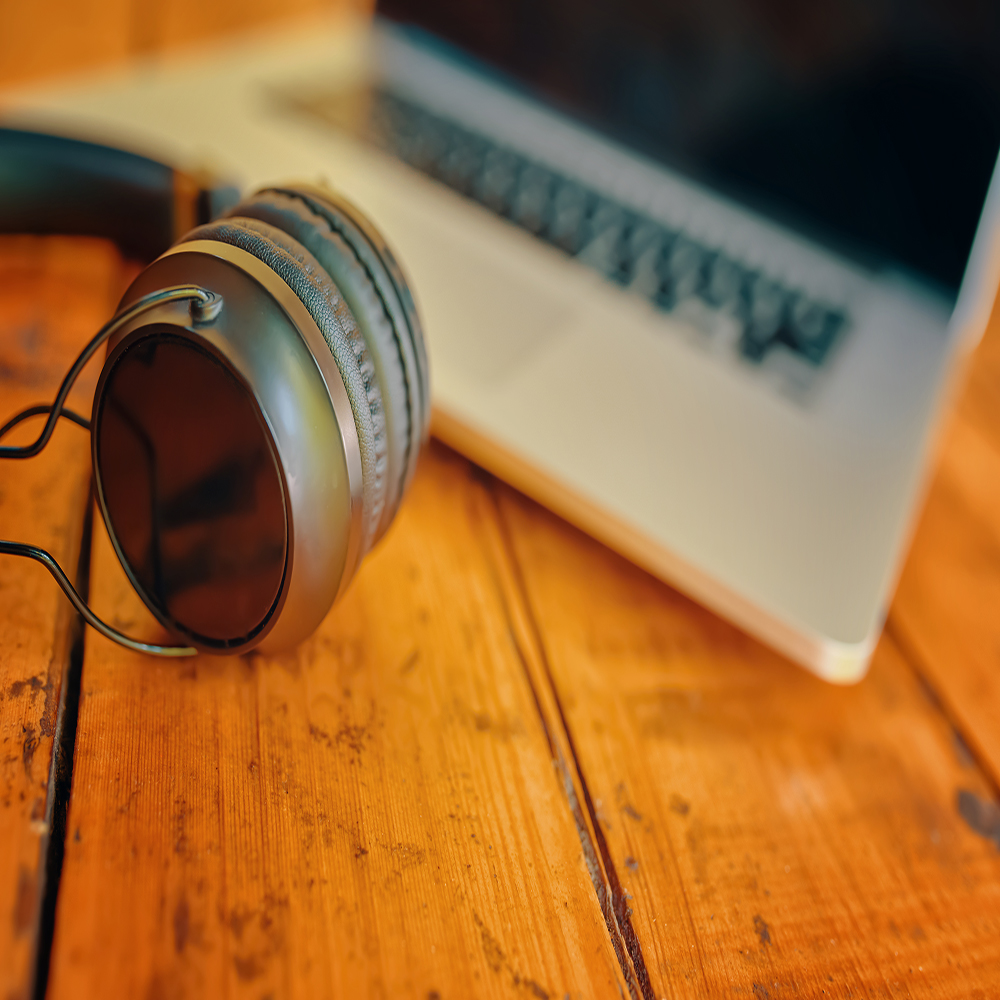 Laptop and wireless headphones on wooden table. Modern gadgets. Workspace of freelance. Grey notebook with black screen and earphones.